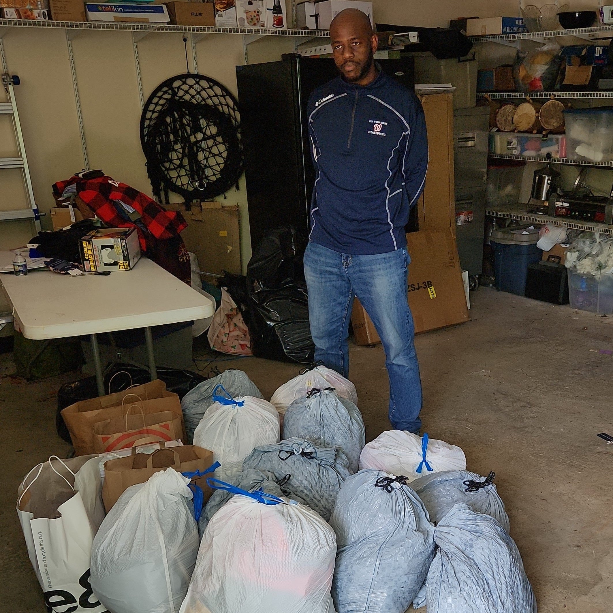 Man standing next to bags of donations in a storage room.